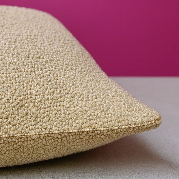 Detalhe macro do tecido bouclé bege do sofá Bloom, com a costura da lateral visível, sobre piso de concreto claro e parede rosa magenta